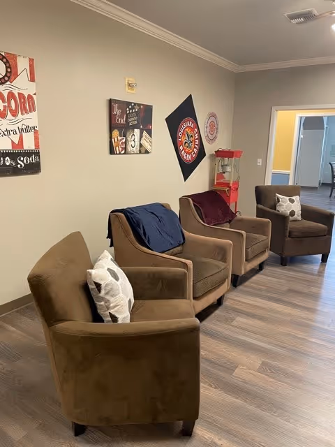 Row of four brown upholstered armchairs with decorative pillows and wall art in a communal seating area.