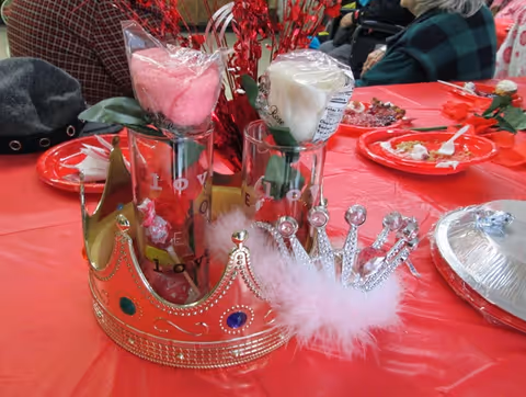 Table centerpiece with decorative crowns, faux roses in vases and red table settings at a communal meal.