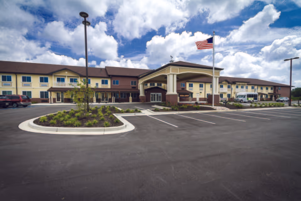Front exterior of Meadow Brook Senior Living with entrance canopy, parking, and American flag.