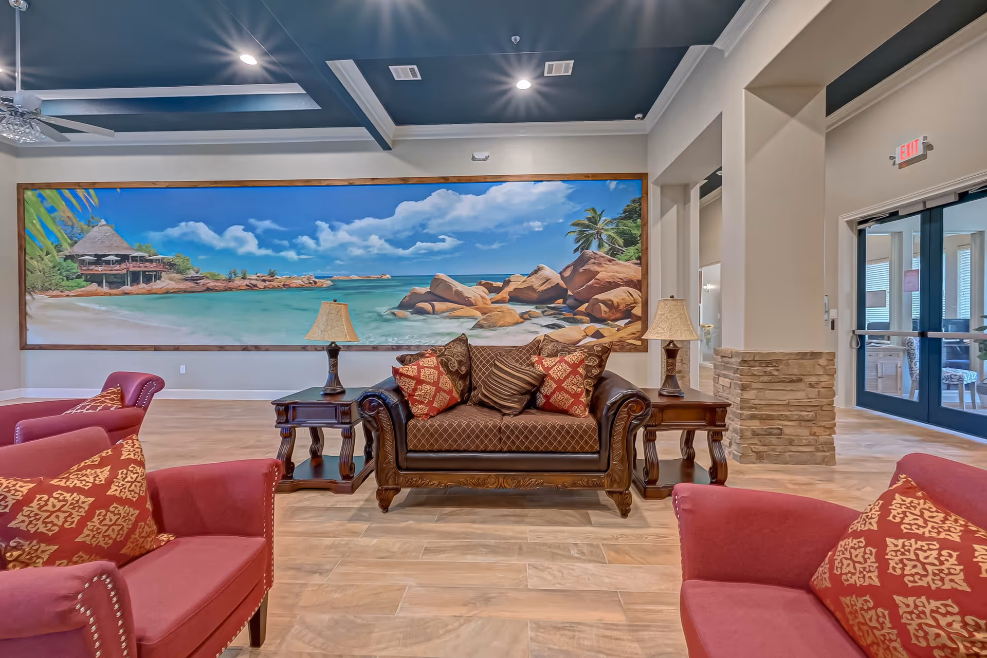Comfortable lounge with a sofa, armchairs and side tables in front of a large tropical beach mural.