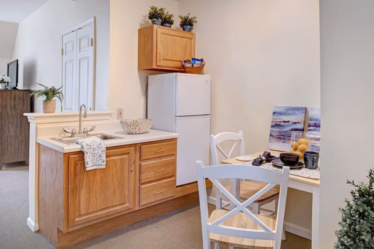 Small kitchenette and dining nook with a sink, refrigerator, wooden cabinets, and a table set for two.