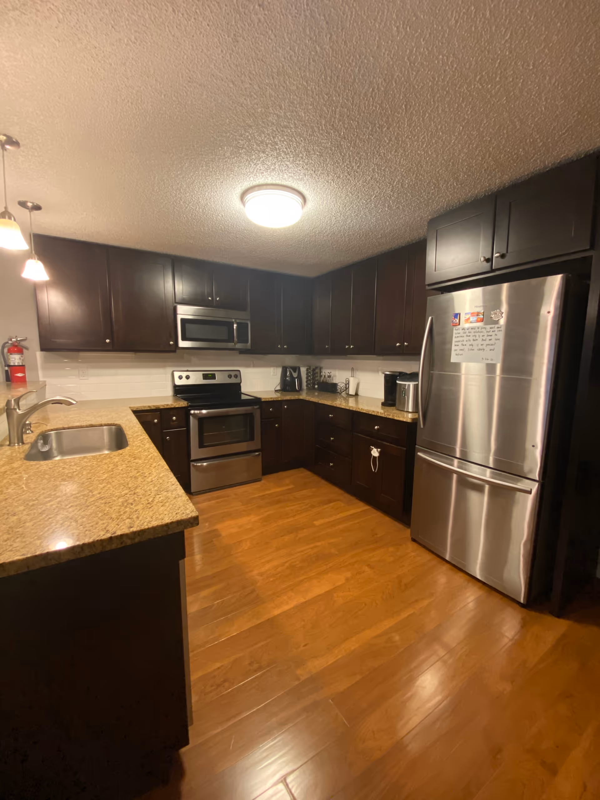 Well-lit kitchen with dark wood cabinets, stainless steel appliances, granite countertops and hardwood floors.