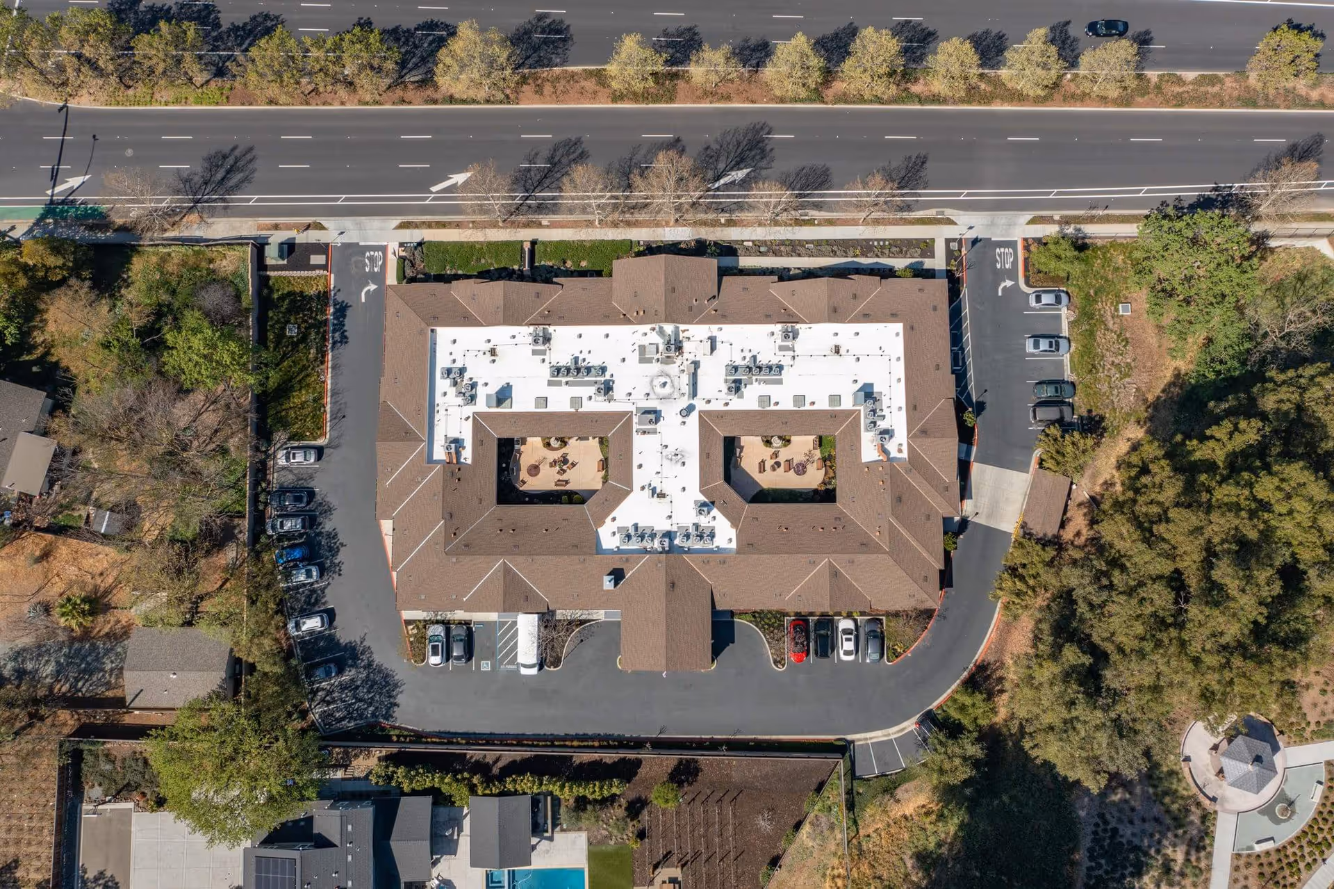 Aerial view of the Sunol Creek Memory Care building showing two central courtyards, surrounding parking areas, nearby road, and trees.