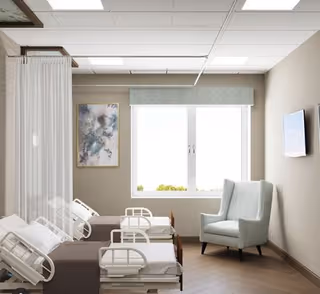 Shared patient room with two hospital beds, a privacy curtain, an armchair, a wall-mounted TV, and a window.