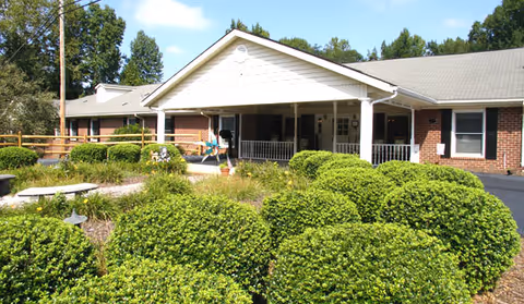 Front exterior of a single-story brick senior living building with a covered entrance and neatly trimmed shrubs.