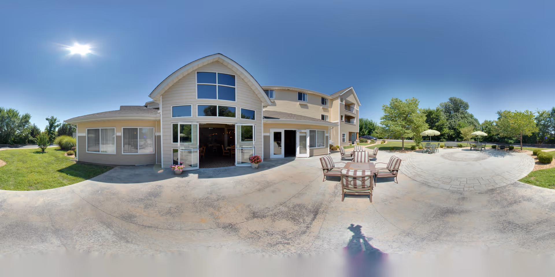 Sunny exterior view of a two-story beige building with large windows, an open patio area and outdoor seating with umbrellas.