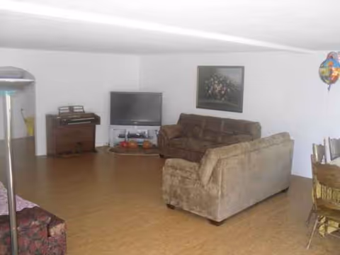 A cozy living room in a senior facility with sofas, TV, piano, and balloons.