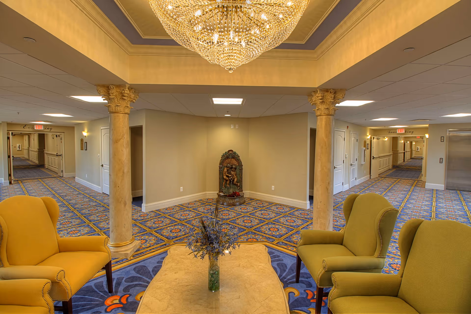Ornately decorated senior living lobby with a chandelier, seating area, decorative columns and patterned carpet.
