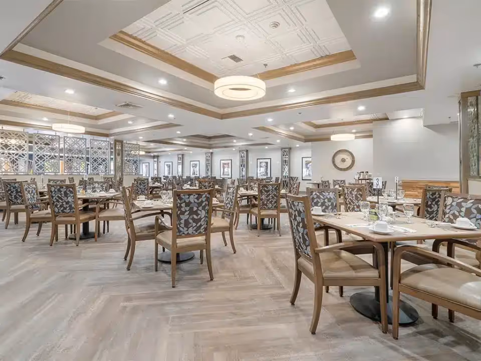 Large bright dining room with multiple set tables and patterned wooden chairs.