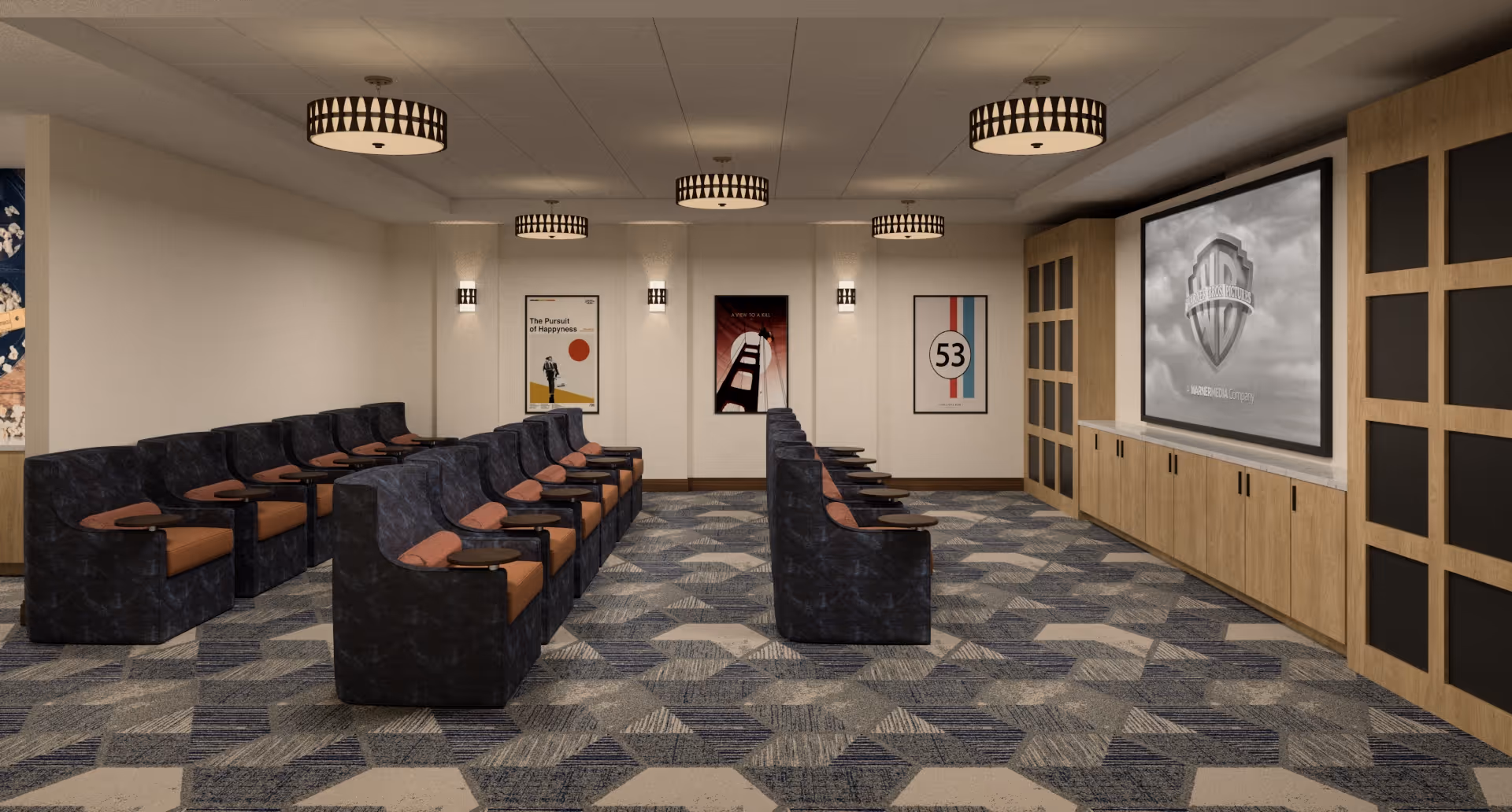 A small theater room with two rows of black cushioned seats with brown armrests and attached small tables, facing a large screen displaying the Warner Bros. logo. The room has patterned carpet flooring, beige walls with three framed movie posters, and modern ceiling lights.