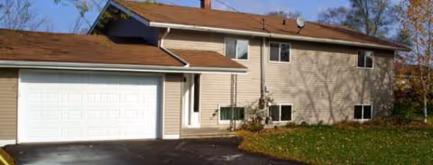 Two-story beige house with attached garage and leaf-covered lawn in autumn.