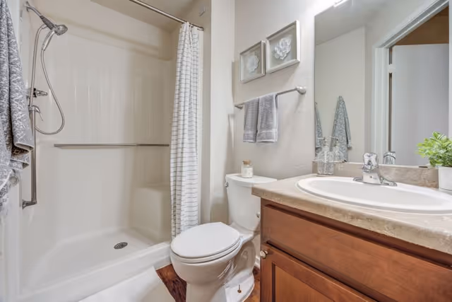 Bathroom with a shower-tub and striped curtain, toilet, sink set in a wooden vanity, and a wall mirror.