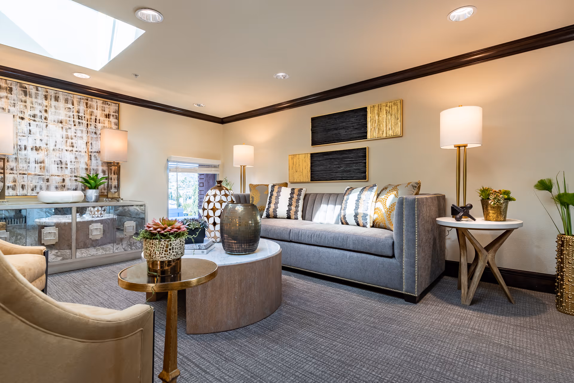 A modern living room in a senior living facility featuring a gray sofa, armchairs, coffee tables, decorative vases and lamps.