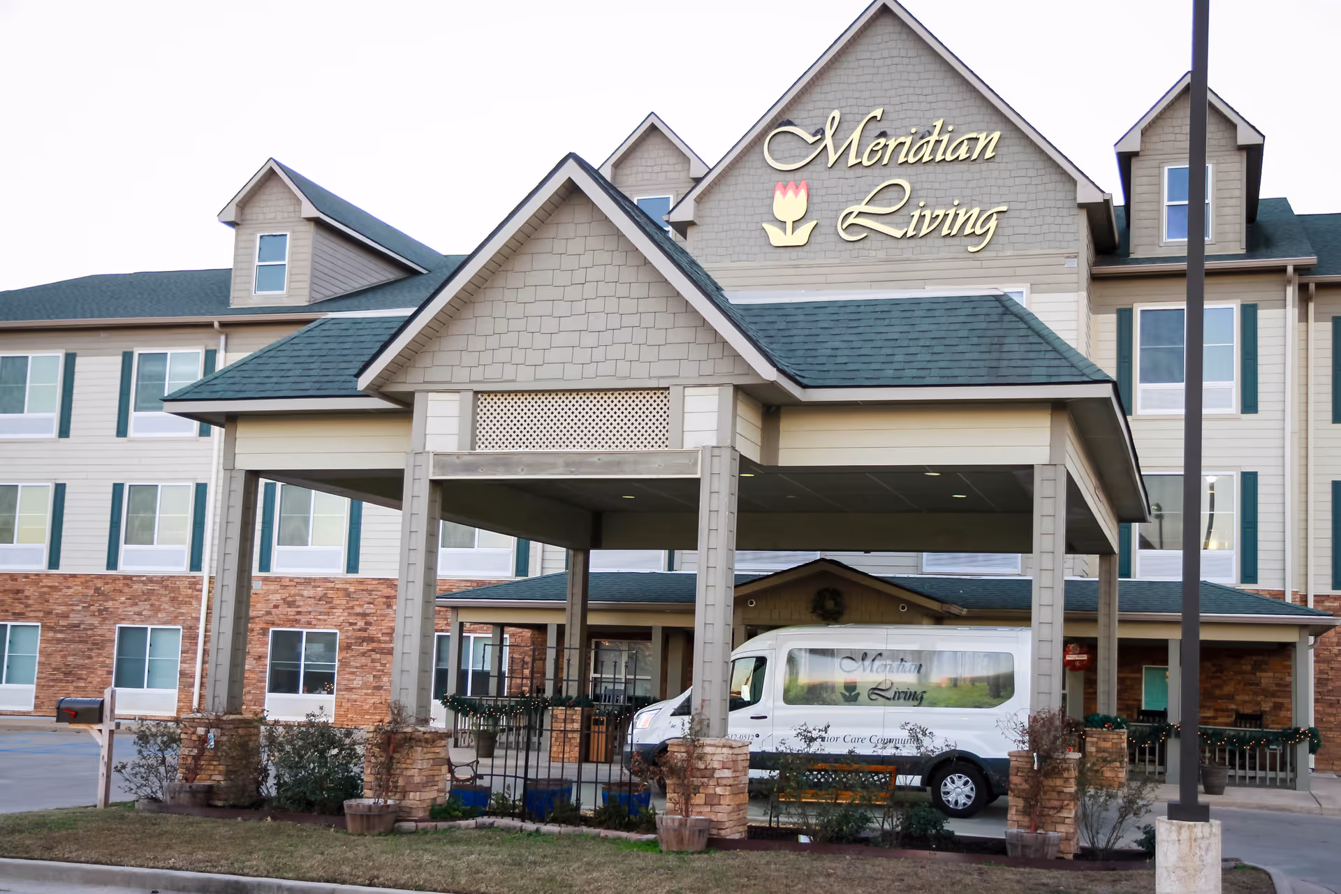 Front entrance of the Meridian Living senior facility with a covered porte-cochere and a branded van parked underneath.