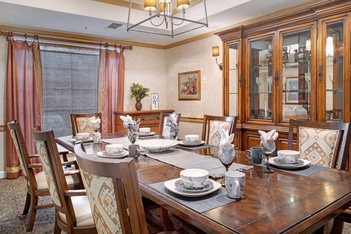 Well-appointed dining room with a set wooden table and chairs, china cabinet, and a curtained window.