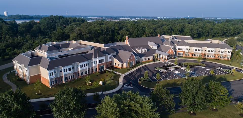Aerial view of Village Point Rehabilitation & Healthcare building surrounded by trees and greenery, with a parking lot and curved driveway in front.