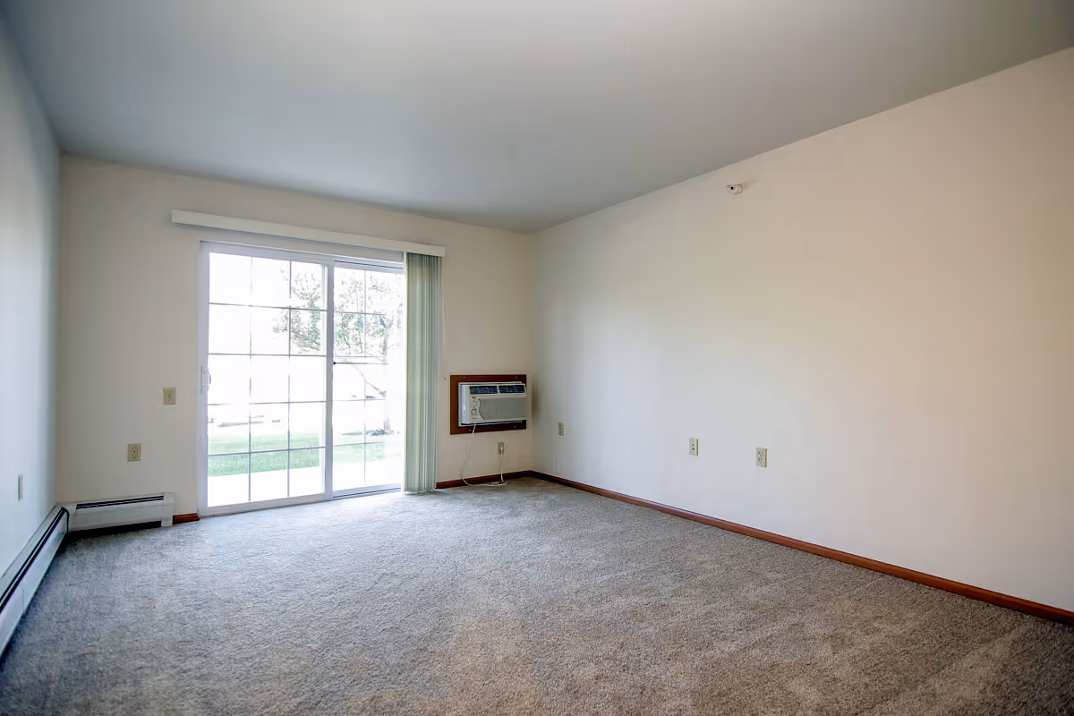Empty room with beige carpet, white walls, a sliding glass door with vertical blinds leading outside, and a wall-mounted air conditioning unit.