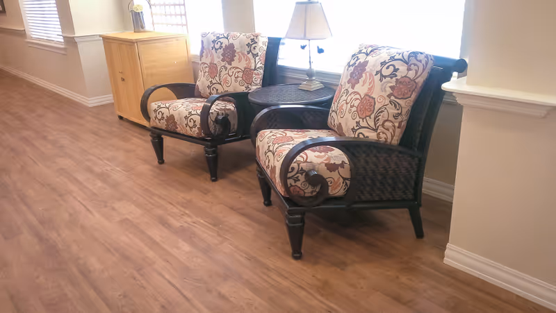 Two patterned armchairs flanking a side table with a lamp in a bright seating area with wood flooring.