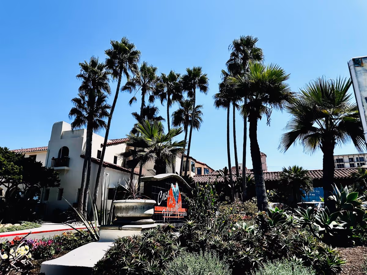 Spanish-style retirement community entrance with palm trees, landscaped gardens and a sign for Casa de Mañana.