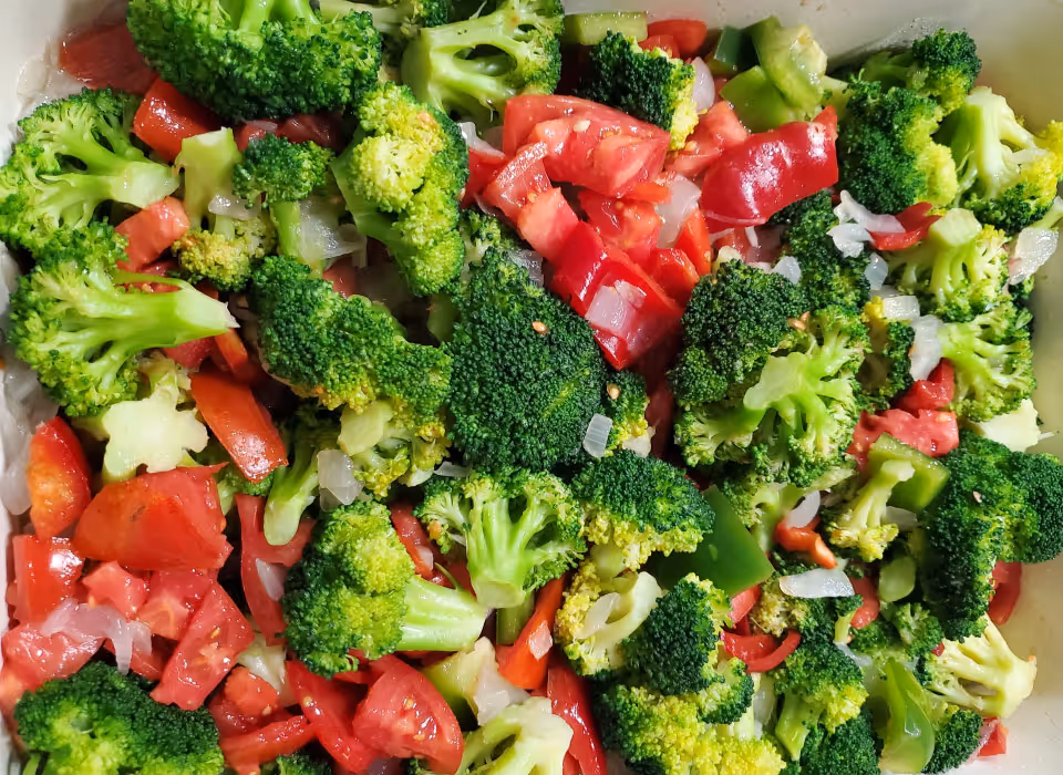 A close-up view of a fresh vegetable mix consisting of chopped broccoli, diced tomatoes, red bell peppers, green bell peppers, and onions.
