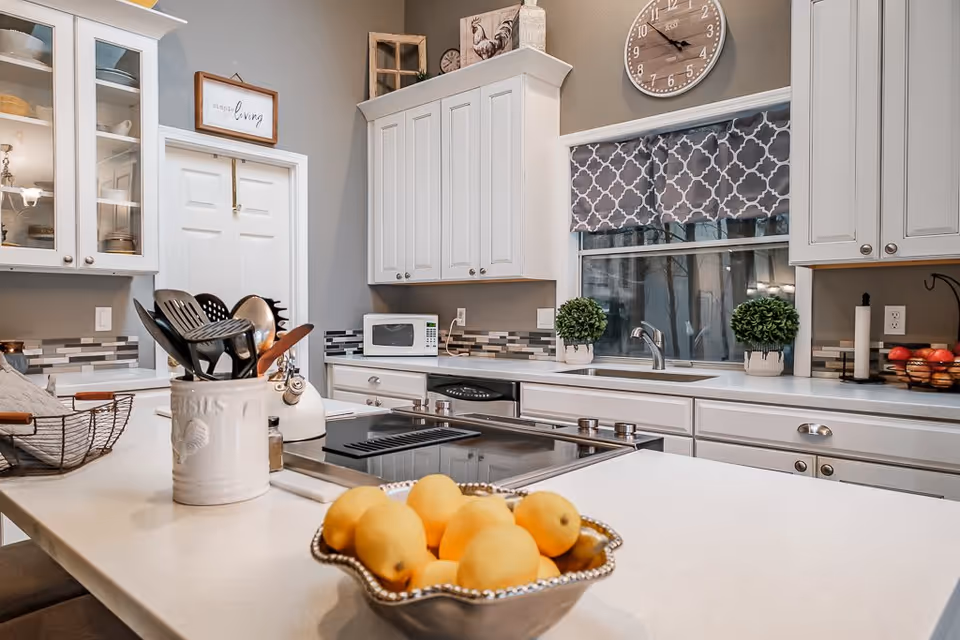 Bright modern kitchen with white cabinetry, a central island holding a bowl of lemons and a utensil holder, and a window above the sink.