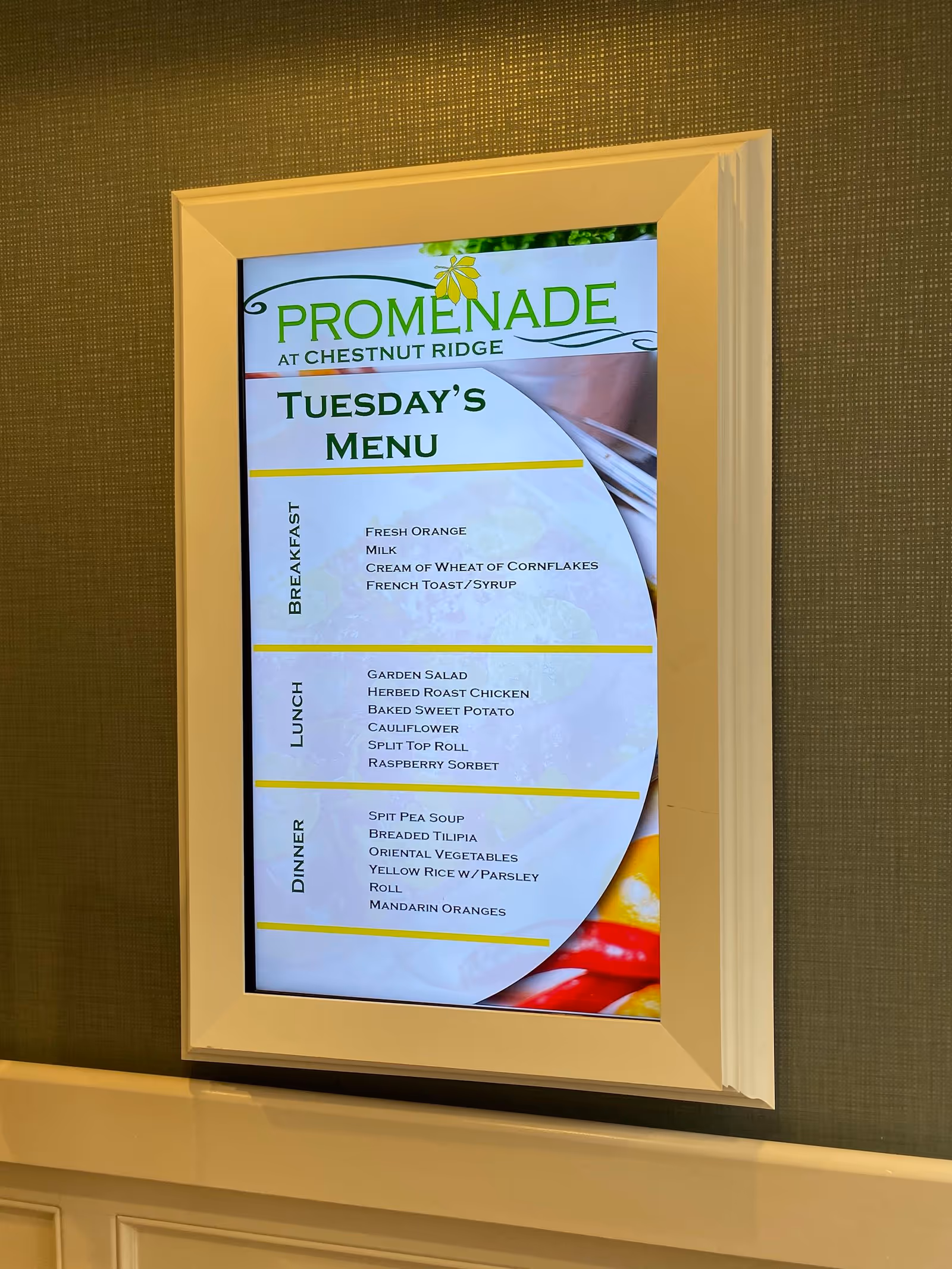 Framed digital display on a wall showing the 'Promenade at Chestnut Ridge' Tuesday's menu.