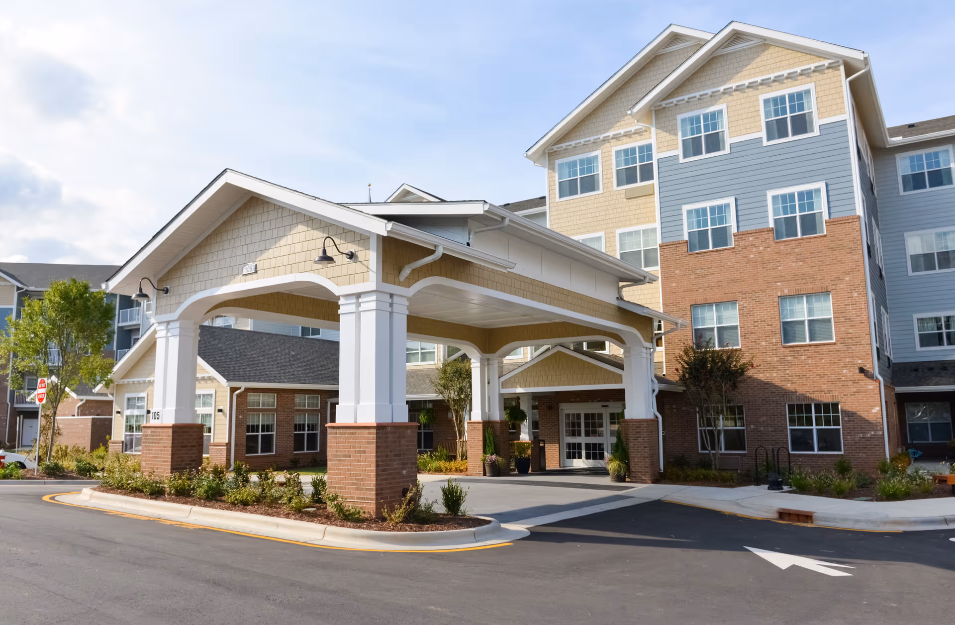 Covered main entrance and porte-cochere of a multi-story senior living building with brick and siding facade.