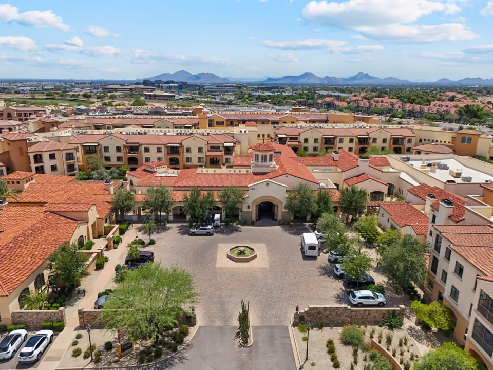 Aerial view of Maravilla Scottsdale's Mediterranean-style senior living complex with a central courtyard and fountain, surrounding parking, and mountains in the background.