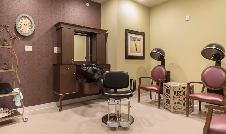 Interior salon area with a styling chair and shampoo sink, plus hooded dryers and seating.