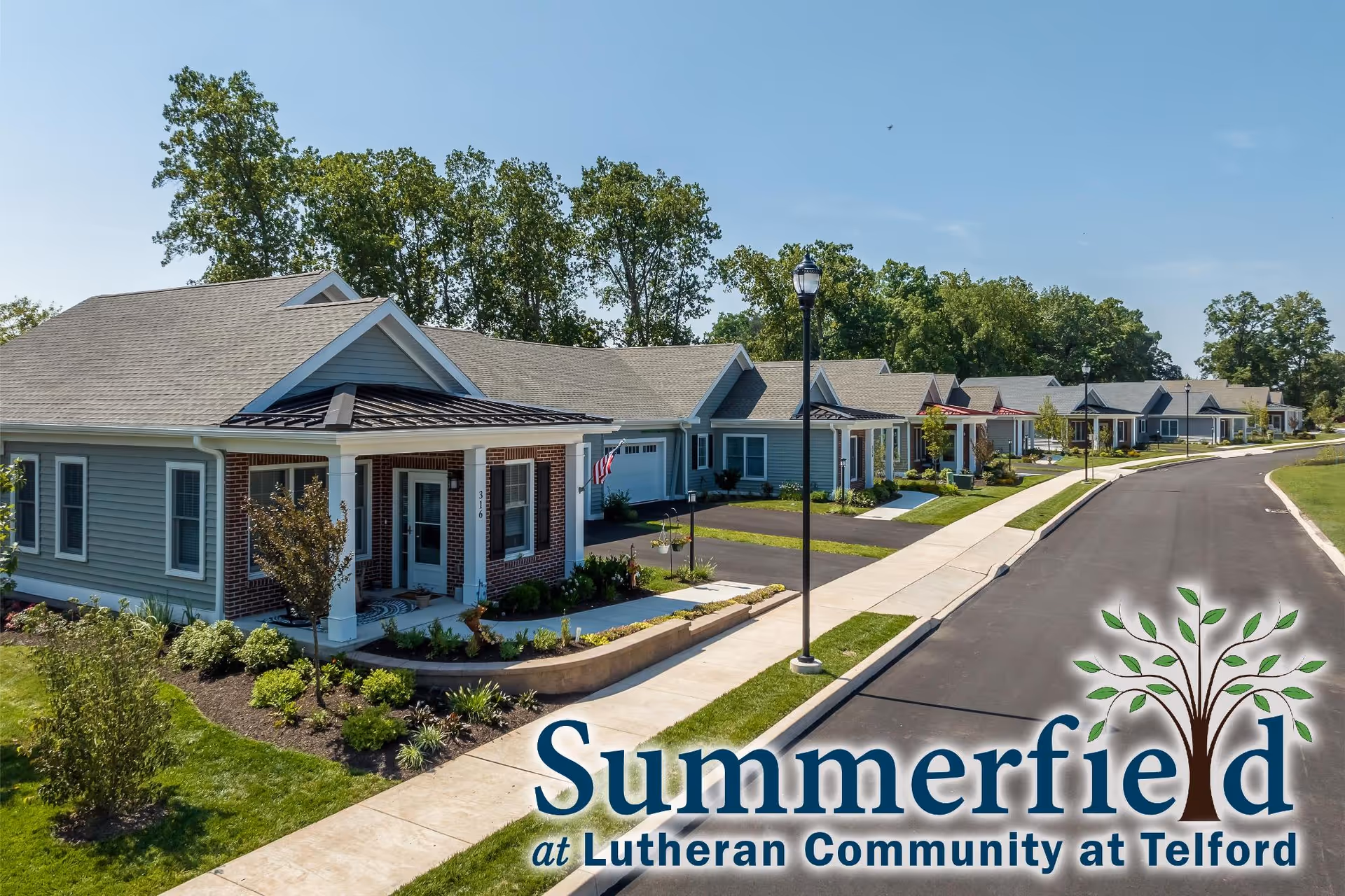 A row of single-story residential homes with front porches and well-maintained landscaping along a paved street under a clear blue sky, part of the Summerfield community at Lutheran Community at Telford.