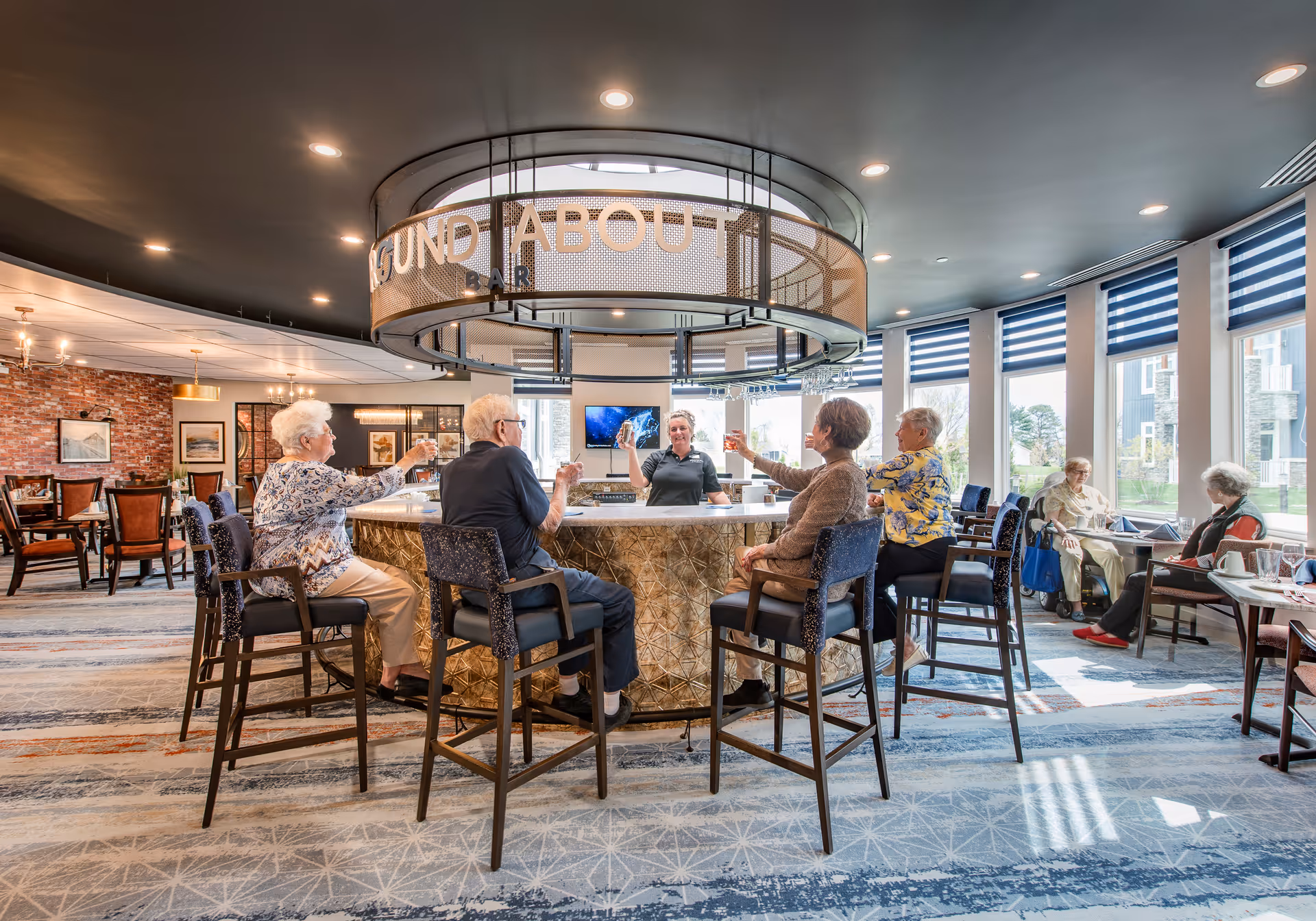 Seniors seated around a circular bar in a bright dining/lounge area with large windows.