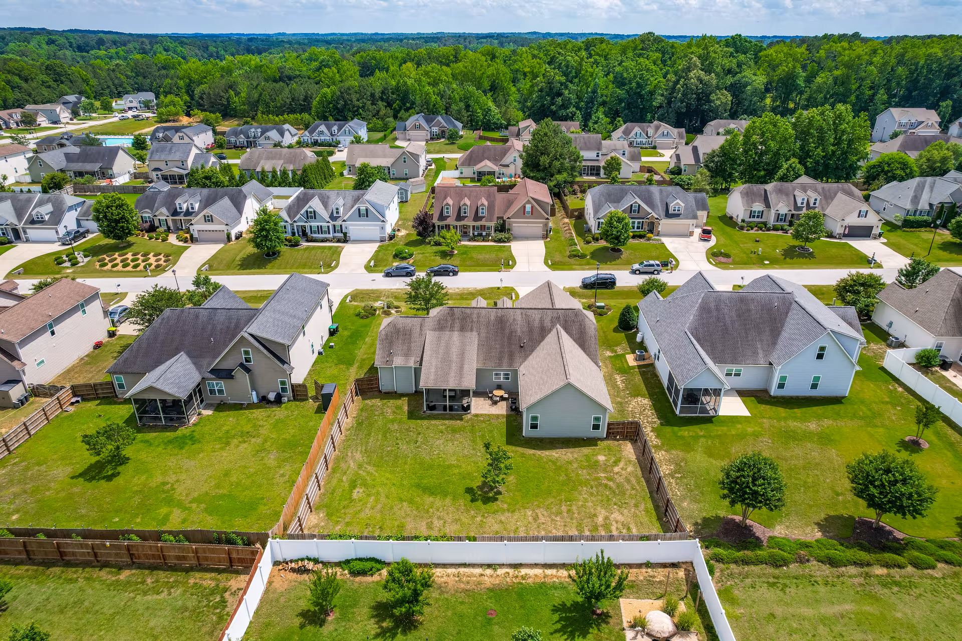 Aerial view of a suburban neighborhood with single-family homes, fenced backyards, and green lawns.