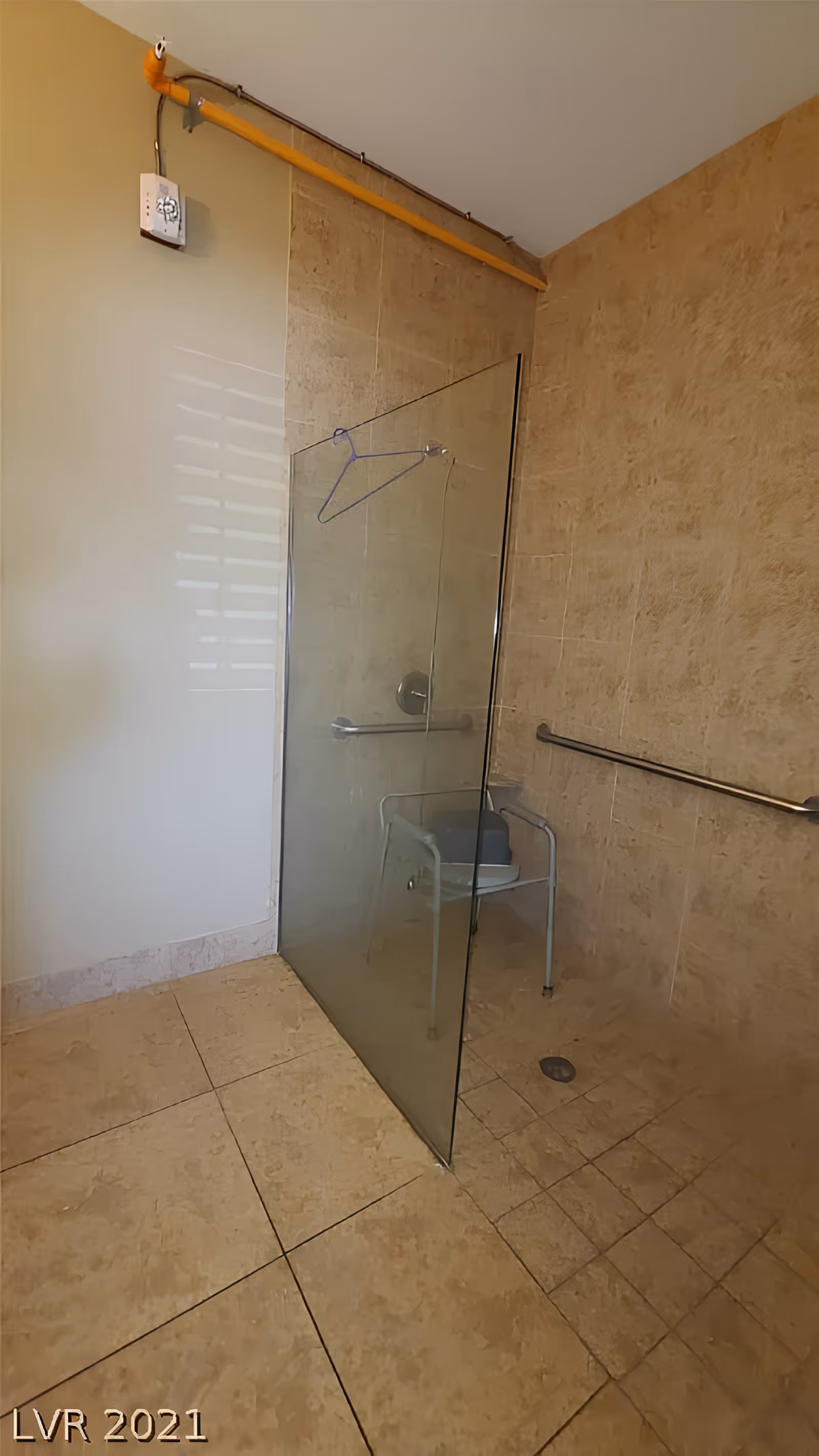 Accessible tiled shower area with a glass partition, shower chair, and grab bars.