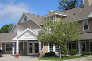 Exterior view of Riverfront Manor facility with entrance, sign, and surrounding landscaping.
