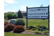 Outdoor view of a landscaped area with bushes, grass, and a sign for Valley View Retirement Community indicating directions to the main entrance and deliveries.