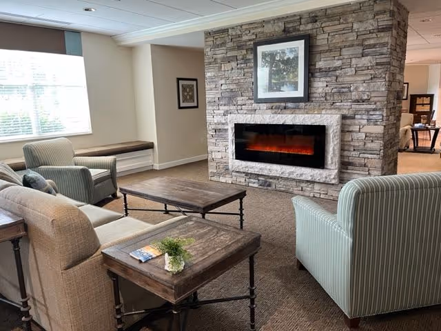 Comfortable common room with sofas and armchairs arranged around a stone fireplace and coffee tables.