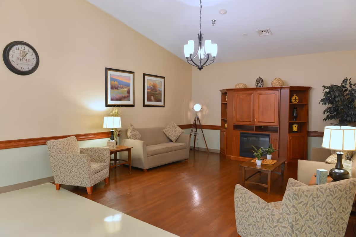 Well-lit communal living room with sofas and armchairs around a coffee table and a wooden entertainment cabinet with a fireplace.