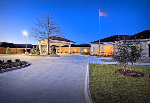 Evening exterior view of Villages on MacArthur with driveway and entrance canopy.