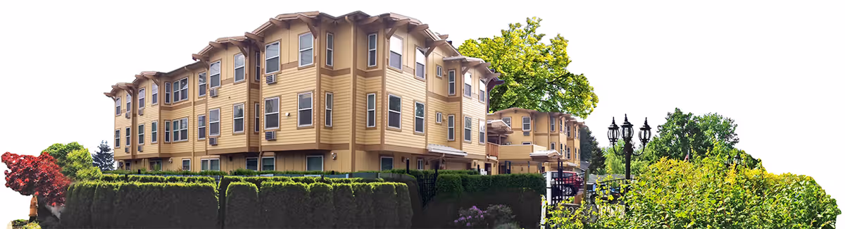 Exterior view of a multi-story senior living facility building with beige siding, multiple windows, and a well-maintained green hedge and trees surrounding the property.
