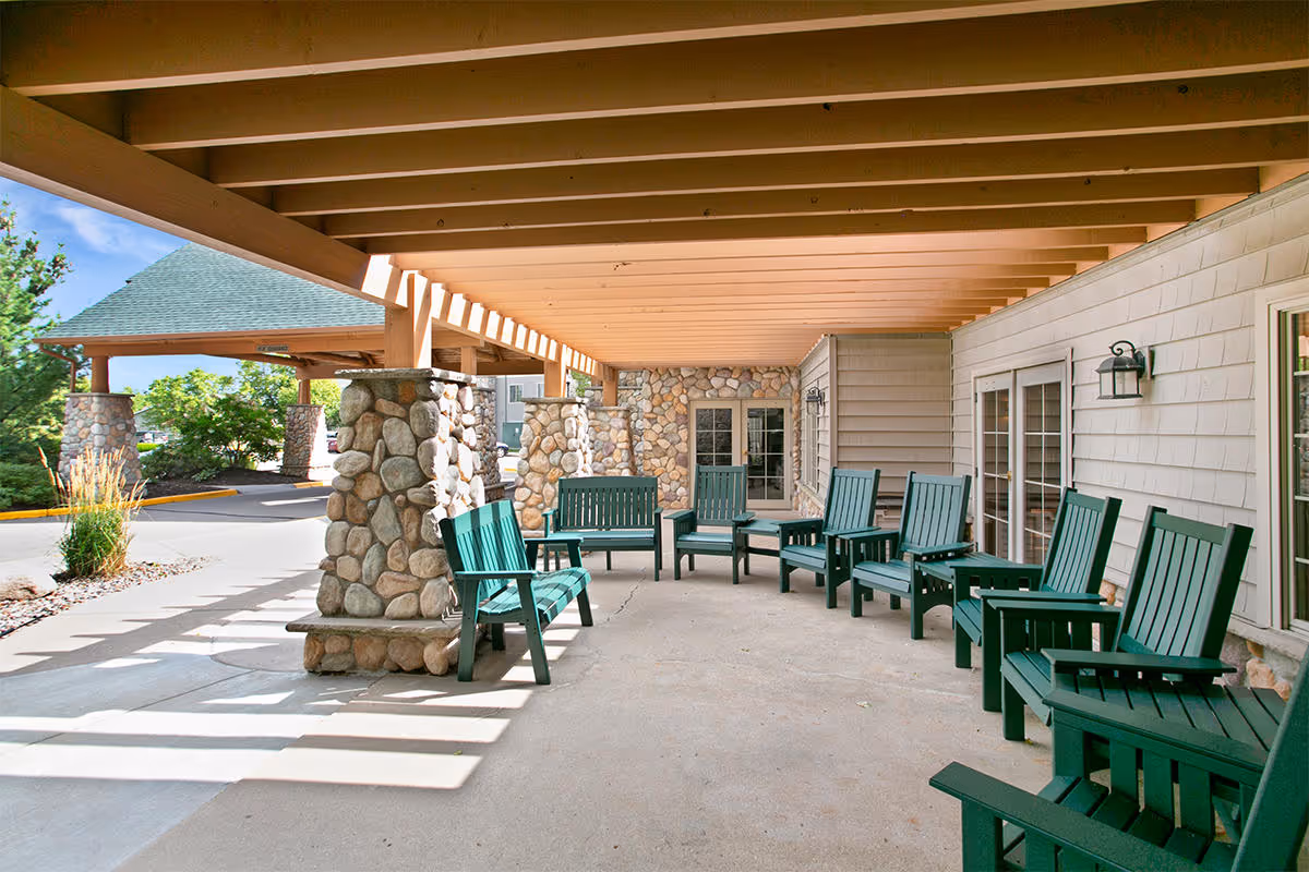 Covered outdoor patio with green wooden chairs and stone columns at the Timber Hills facility.