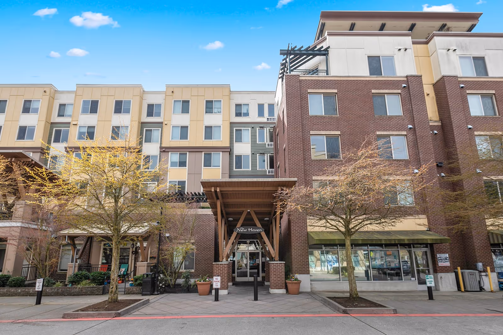 Exterior view of SHAG's New Haven Apartments building with a covered entrance, trees with early spring foliage, and a clear blue sky.