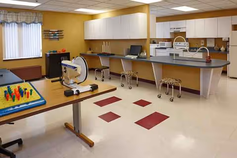 Senior care center recreation area with a kitchen, counter, stools, and play mat in foreground.