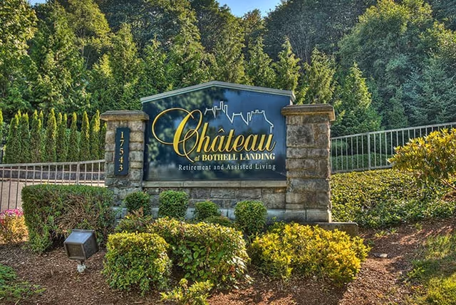 Stone entrance sign reading "Chateau at Bothell Landing Retirement and Assisted Living" surrounded by shrubs and trees.