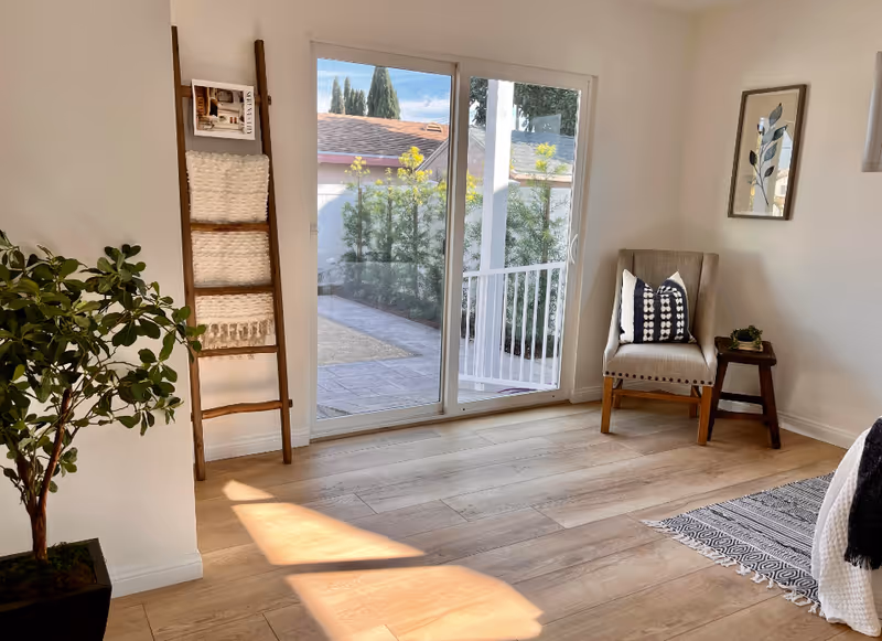 Bright interior living area with a sliding glass door to a patio, chair, and plant.