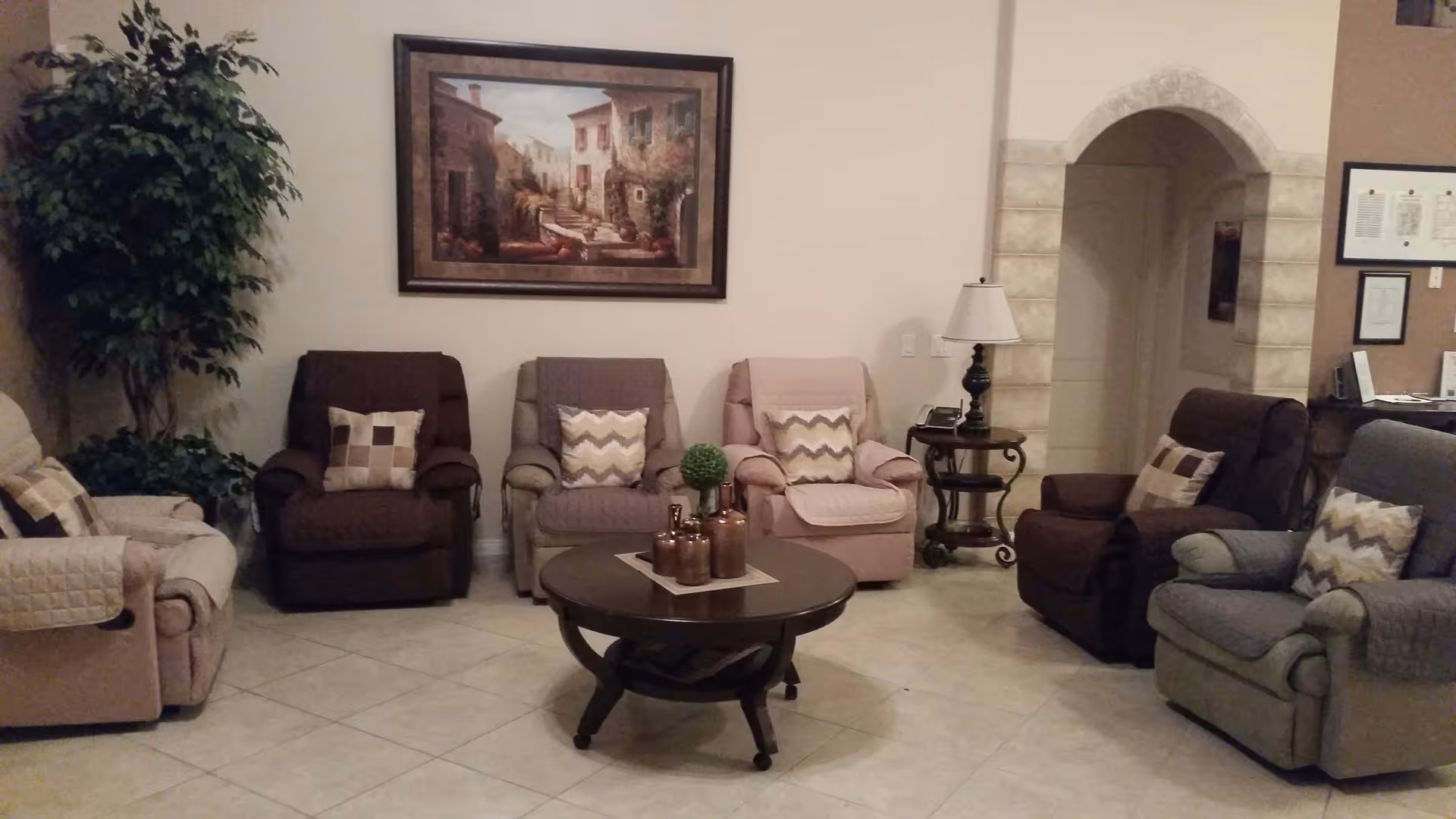 Living room with multiple upholstered recliners arranged in a semicircle around a round coffee table, a framed painting on the wall, and an archway.