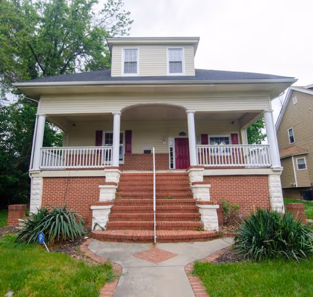 Two-story brick and siding house with a wide front porch, central brick steps, and white columns.