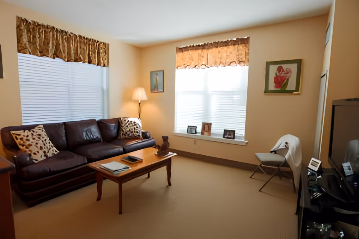 Bright living room with a leather sofa, coffee table, TV and a window ledge displaying framed photos.