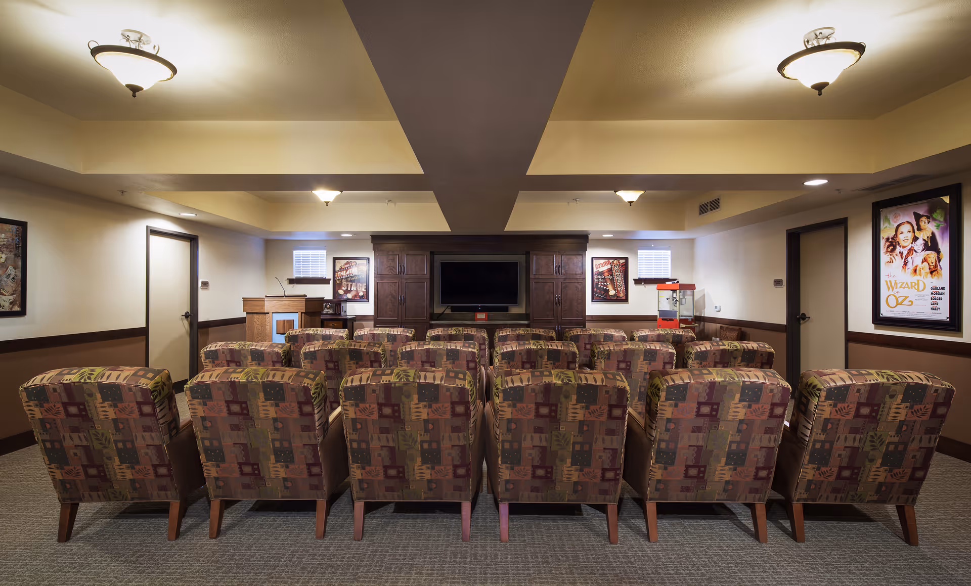 Small screening room with rows of patterned armchairs facing a TV, media cabinet and popcorn machine.