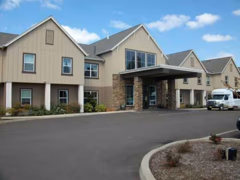 Senior living facility exterior with front entrance canopy, driveway, and parked vehicle.
