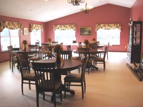 Pink-walled dining room with round tables, chairs, and floral centerpieces.